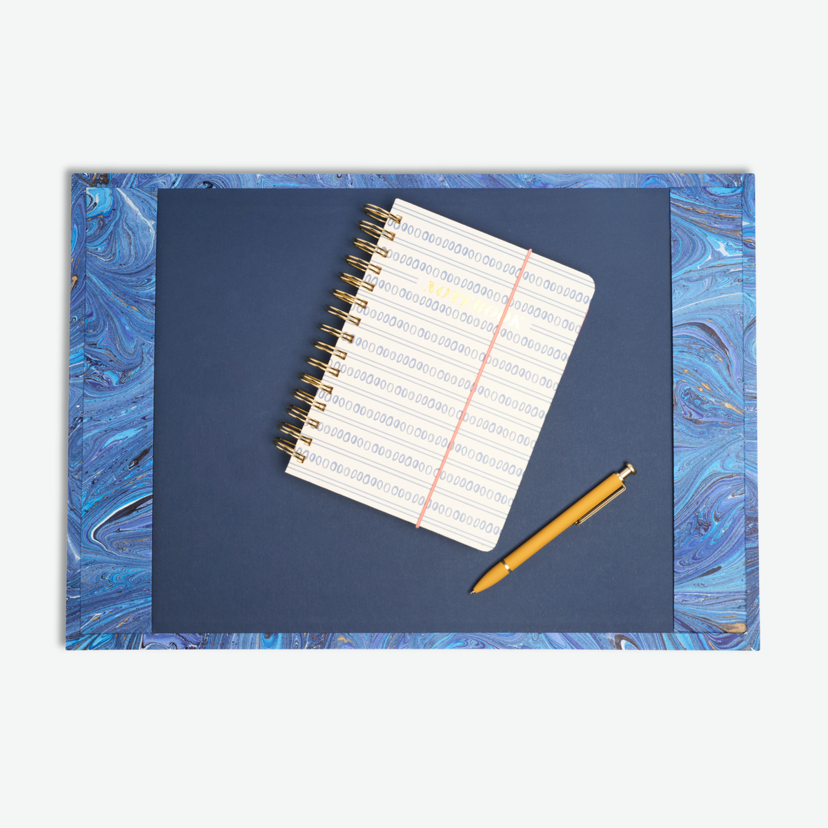 Marbled desk pad in Blue styled on a desk with a notebook and pen resting on top